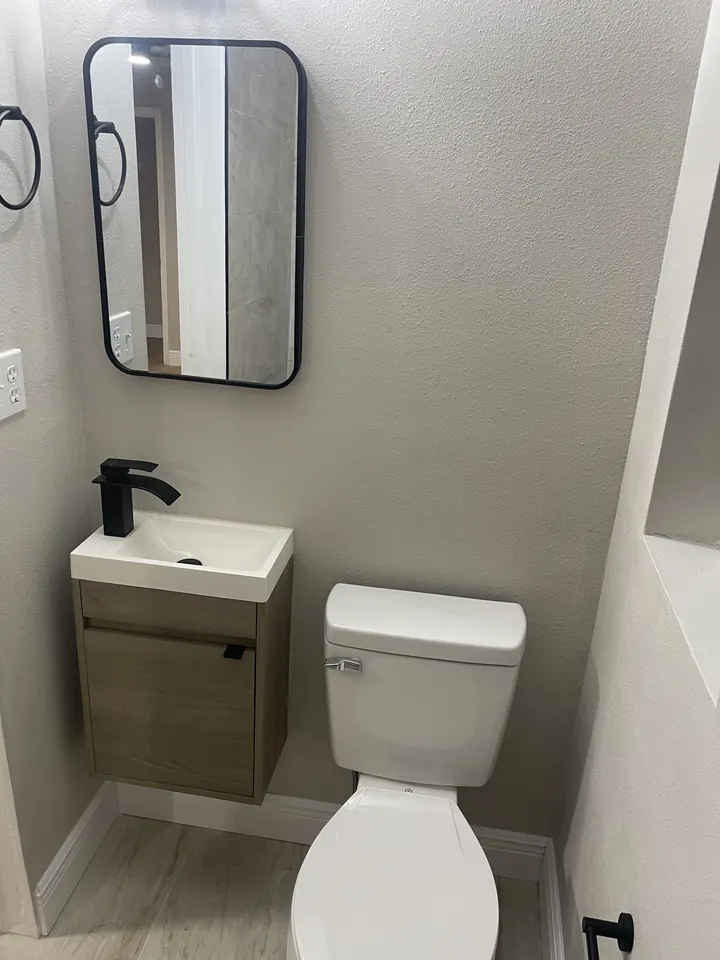 Compact bathroom remodel with a wood vanity, round mirror and black fixtures